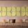 Hush Wall Mounted Acoustic Panels in green and beige, arranged on a pink wall above modern chairs and tables.